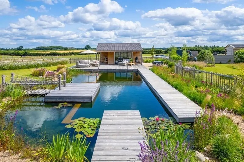 Grote zwemvijver met houten vlonders, natuurlijke oevers en landelijk uitzicht bij een luxe buitenverblijf